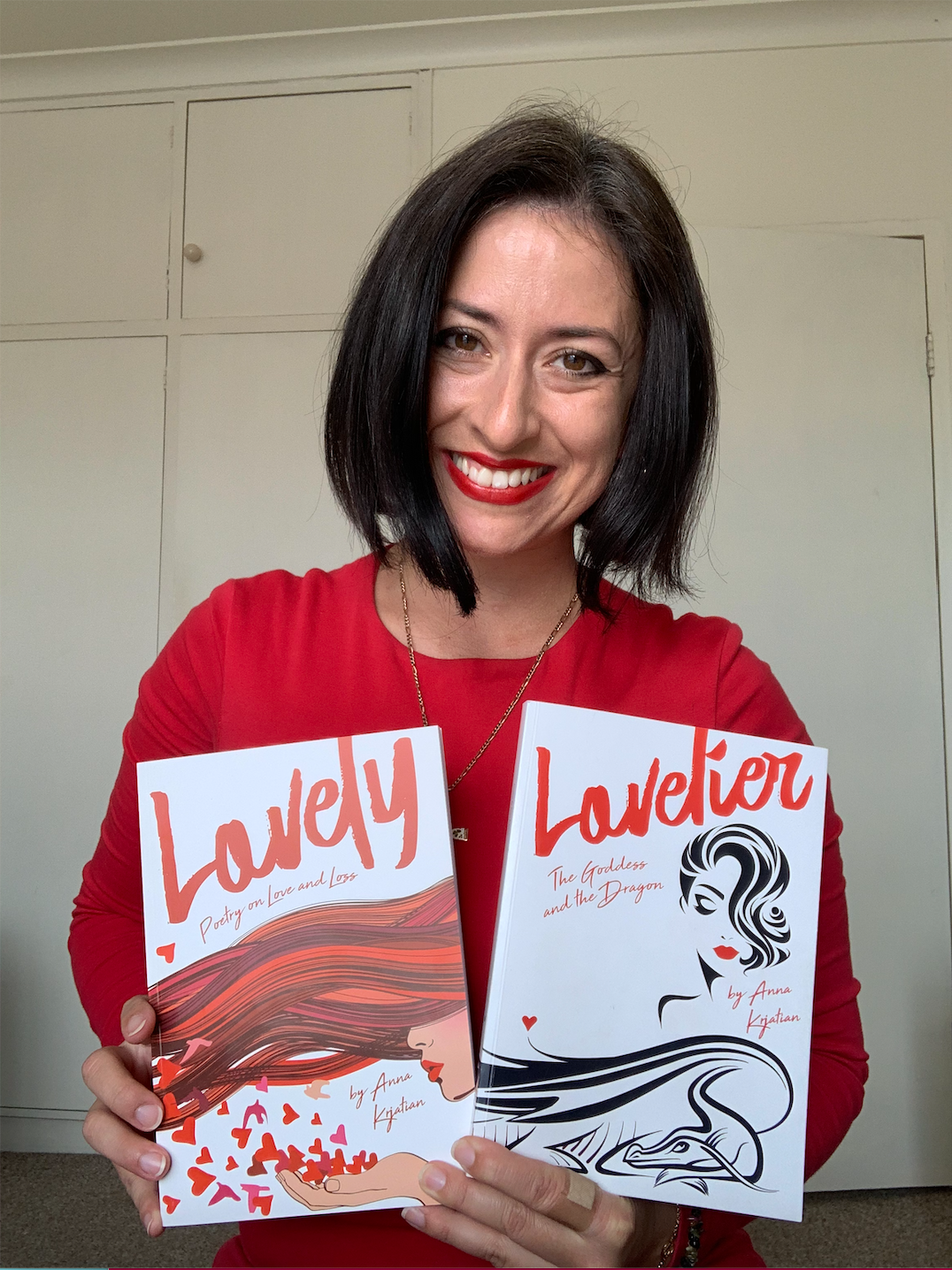 Anna Krjatian, author, biohacker,  entrepreneur and found of "The Butterfly" wears a red dress, and holds two books she's written: "Lovely - Poetry on Love and Loss" and "Lovelier - The  Goddess and The Dragon".