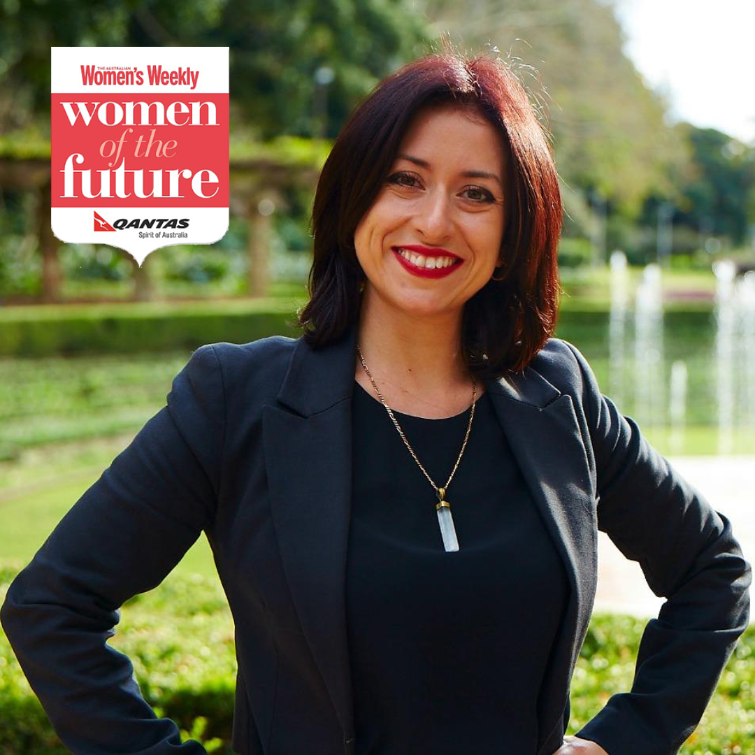 Anna Krjatian standing in a power post - with hands on her hips, with a fountain and trees behind her and the logo for "Women's Weekly Women of the Future and Qantas International" in the top left hand corner.